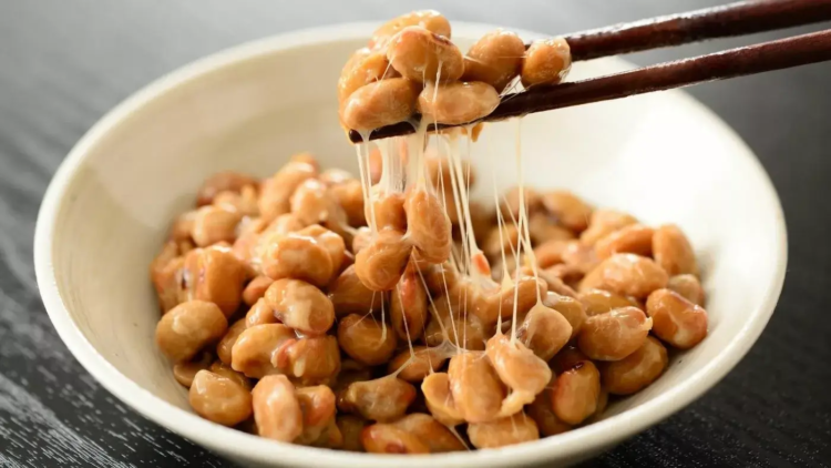 homemade natto picked up by chopsticks in a bowl