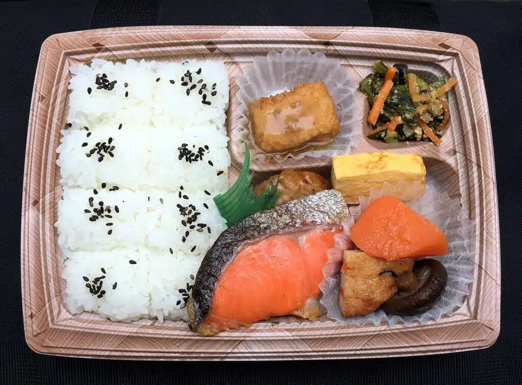 Japanese bento box with grilled salmon, tamagoyaki, rice with black sesame, simmered vegetables and spinach